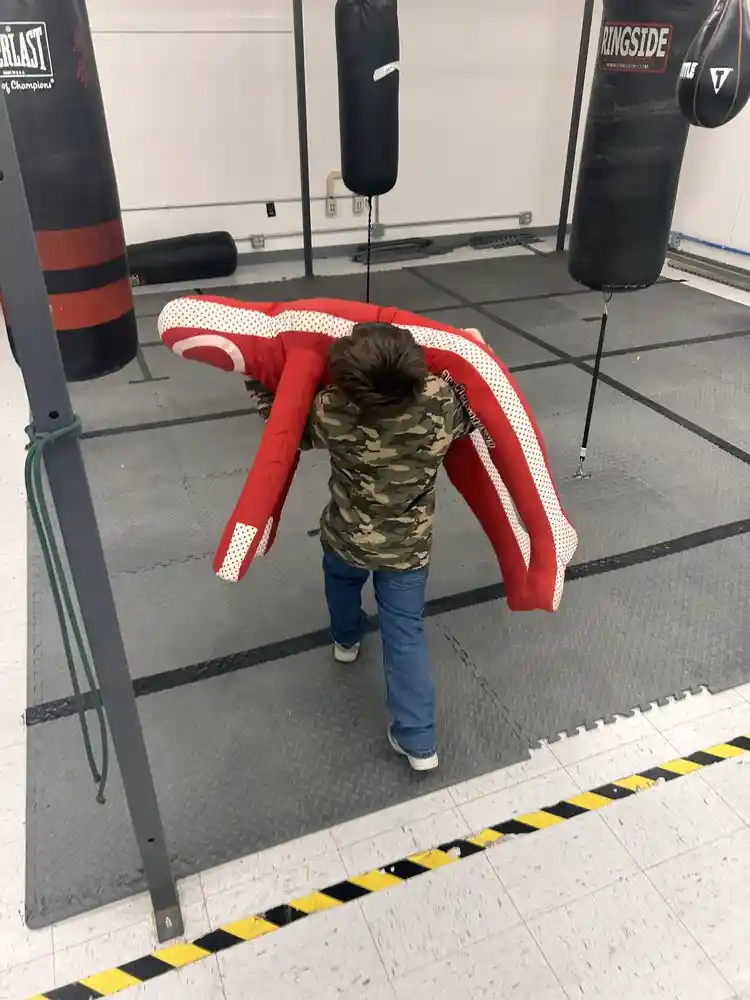 Legacy Boxing youth boxer carrying a 70-pound training dummy